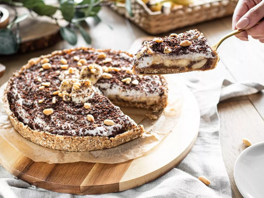 wegańska tarta banoffee pie z kawałkiem na złotej łopatce do ciasta na drewnianej paterze - Wszystkiego Słodkiego