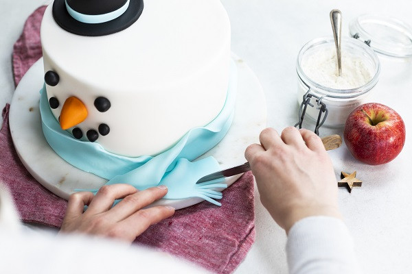 Przyklejanie błękitnego szalika z frędzlami niebieskiego fondantu
