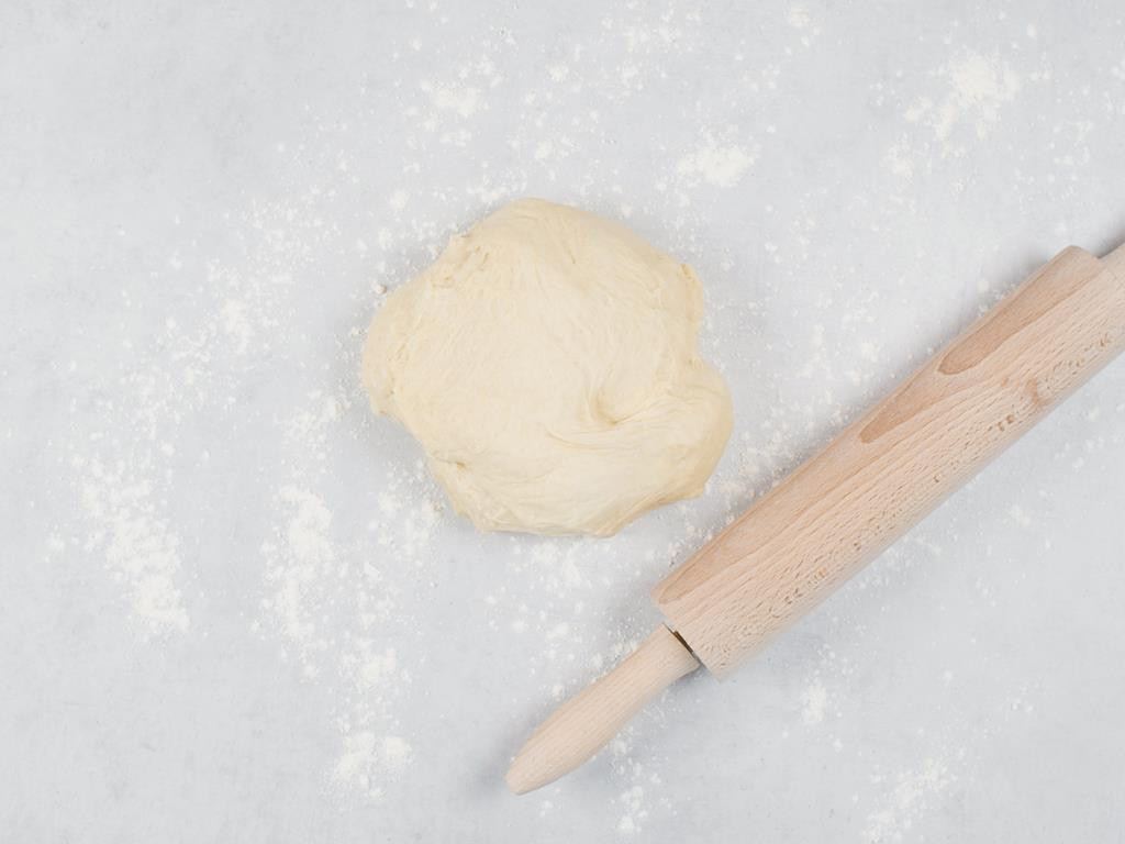kula ciasta drożdżowego na blacie oprószonym mąką,  obok wałek drewniany