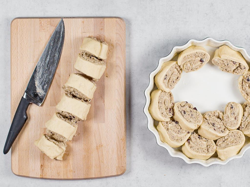 Ciasto drożdżowe z białym makiem zwinięte w roladę i pokrojone na 3 cm plastry na desce, obok plastry ciasta ułożone w formie do tarty