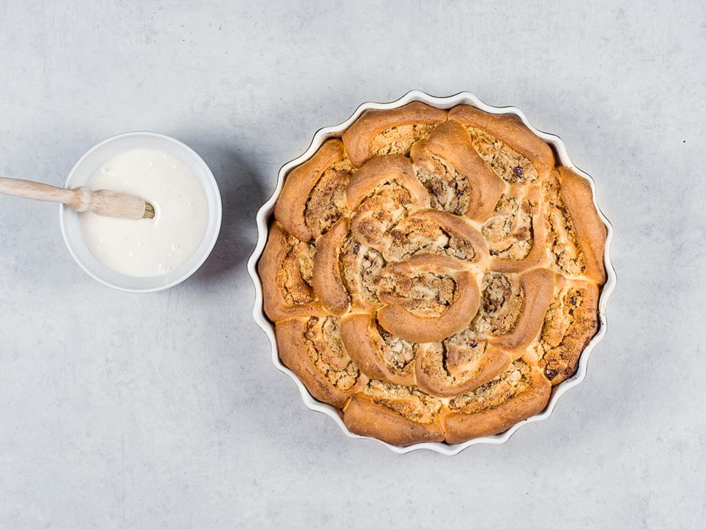 Upieczone drożdżowe ślimaczki w formie do tarty, obok lukier w miseczce