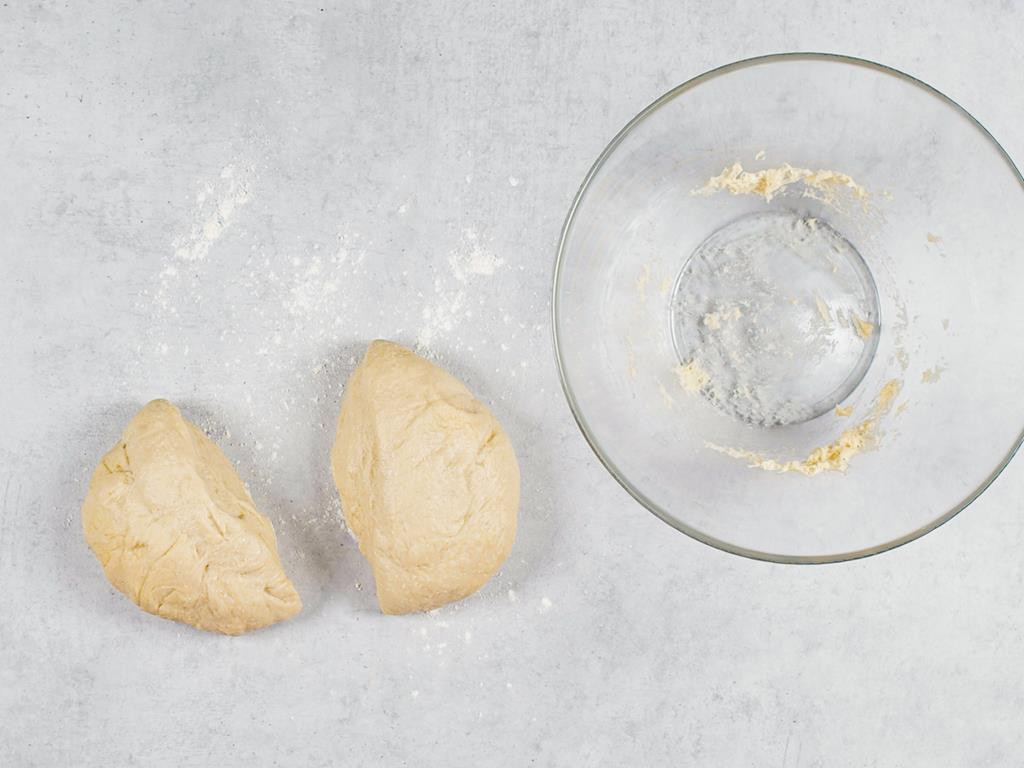 Zagniecione ciasto drożdżowe podzielone na dwie części obok szklanej miski