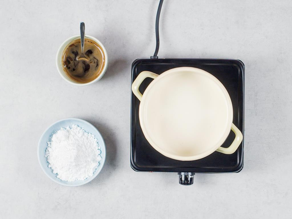 Śmietanka w garnku na palniku, zaparzona kawa w filiżance, cukier puder w miseczce