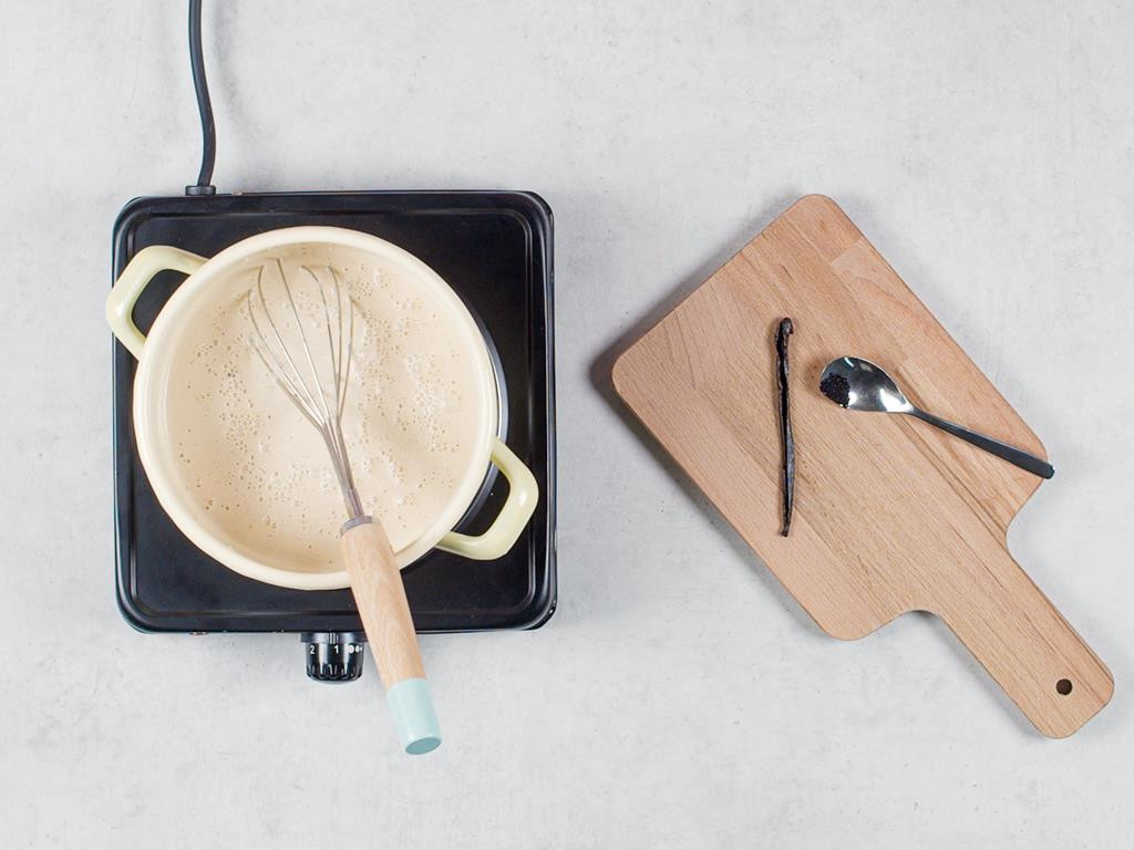 Podgrzana z kawą i cukrem pudrem śmietanka w garnku na palniku, nacięta laska wanilii na deseczce