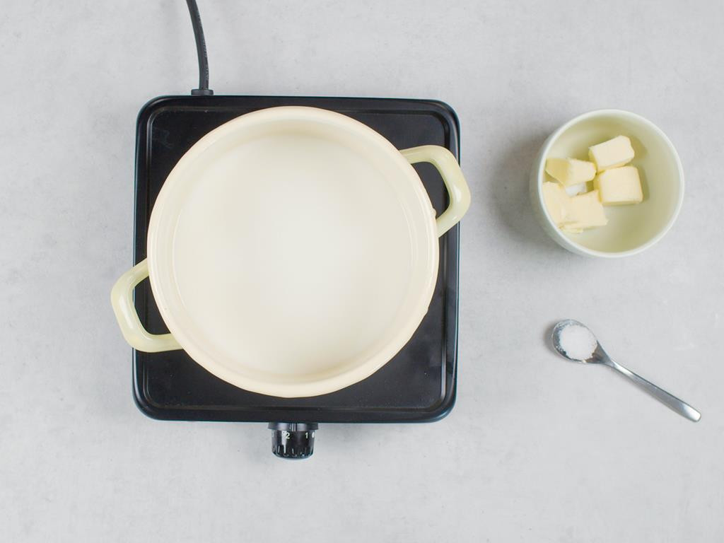 Mleko z wodą w garnku na palniku, masło pokrojone w kostkę w miseczce, łyżeczka z solą