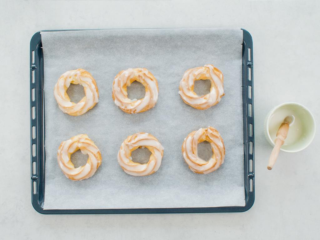 Polukrowane lukrem cytrynowym pieczone pączki hiszpańskie, lukier w miseczce z pędzelkiem