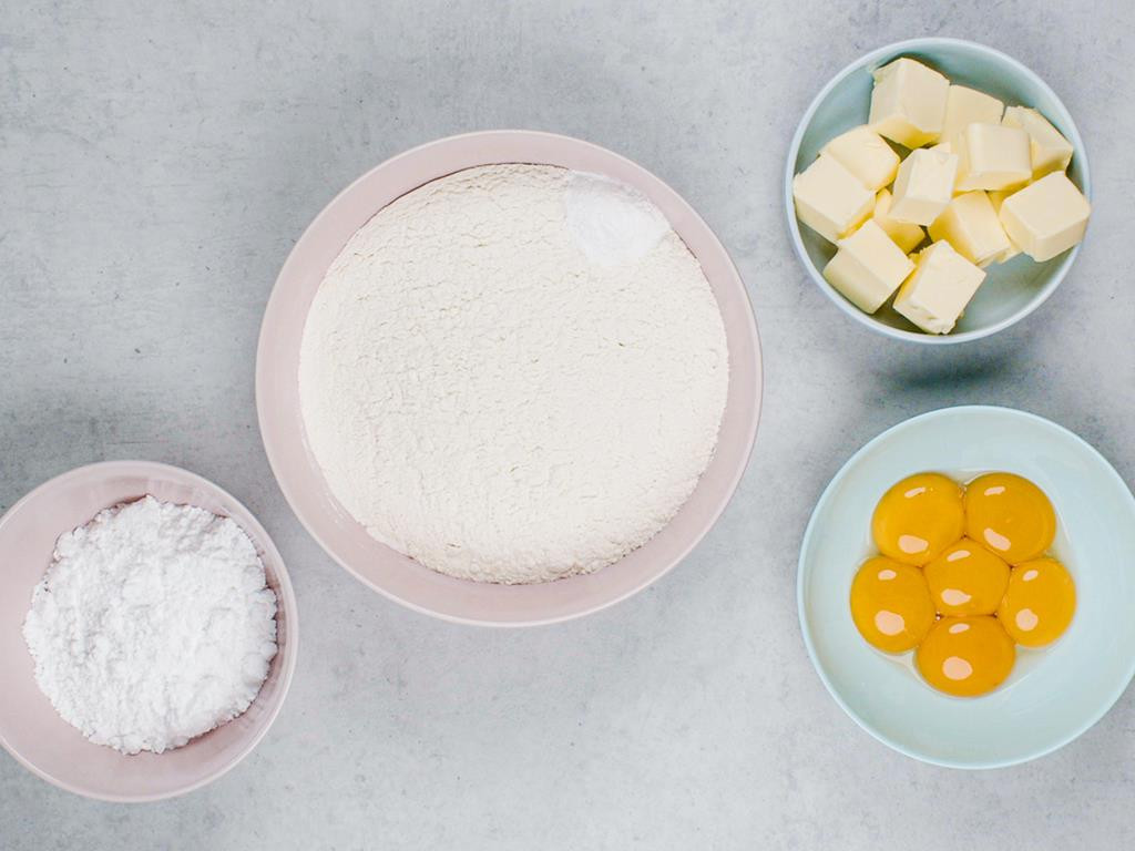 Mąka, proszek do pieczenia, cukier puder, masło pokrojone w kostkę i żółtka w osobnych miseczkach