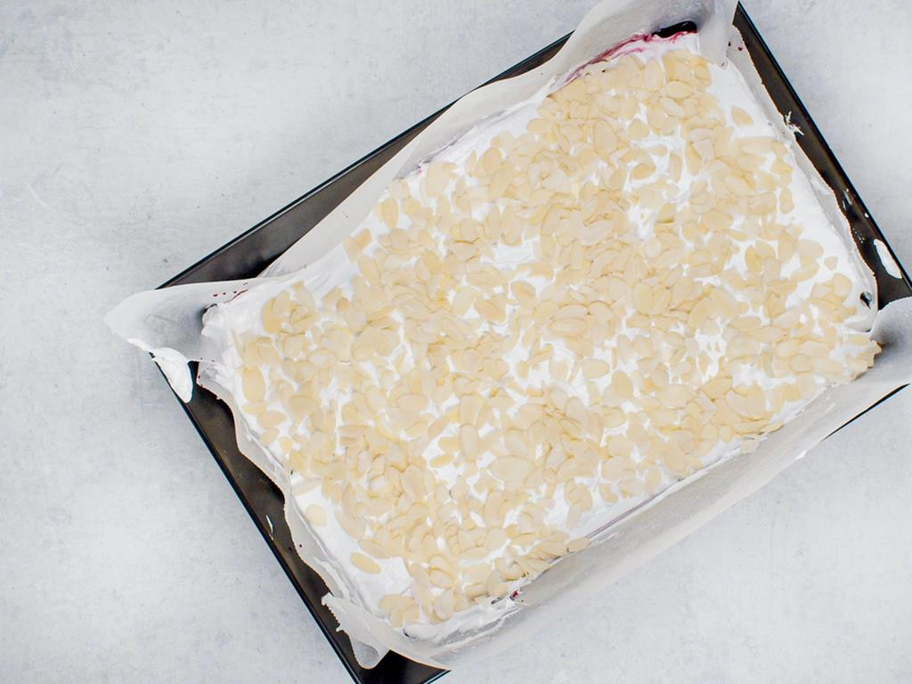 Ciasto z dżemem, pianą z białek i płatkami migdałowymi przed pieczeniem