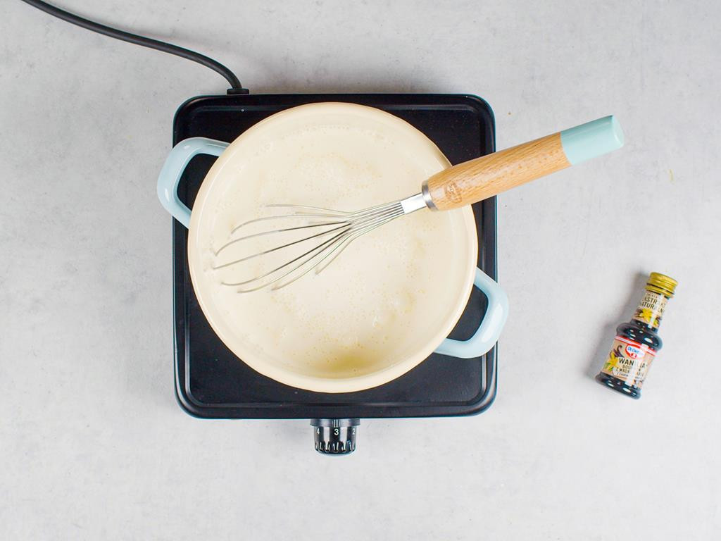 Śmietanka, mleko, cukier i ekstrakt waniliowy Dr. Oetkera w garnuszku z rózgą kuchenną postawionym na palniku