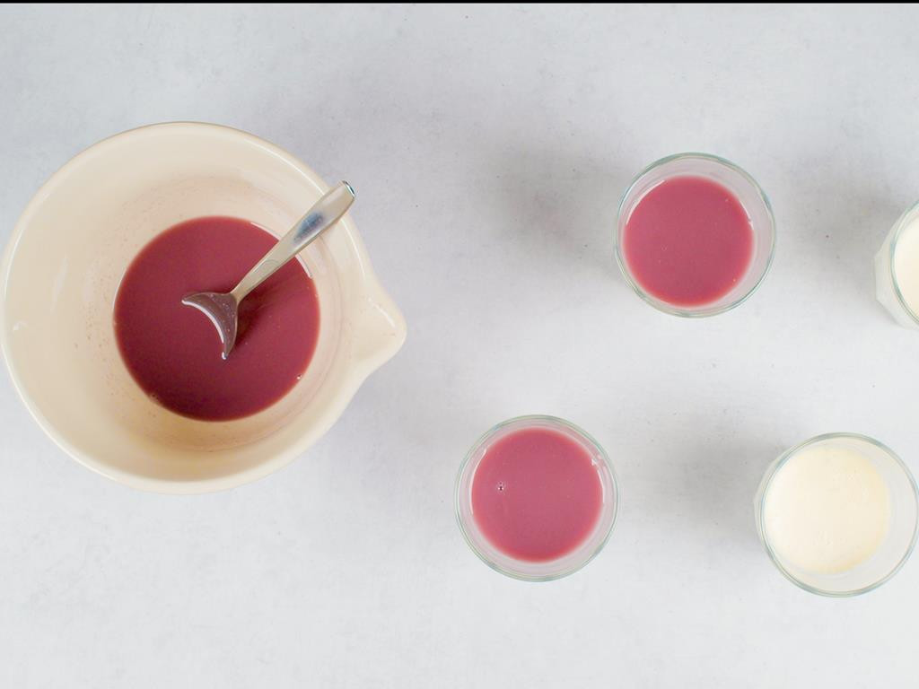 Tężejąca galaretka z granatu rozlana do szklanek z deserem panna cotta