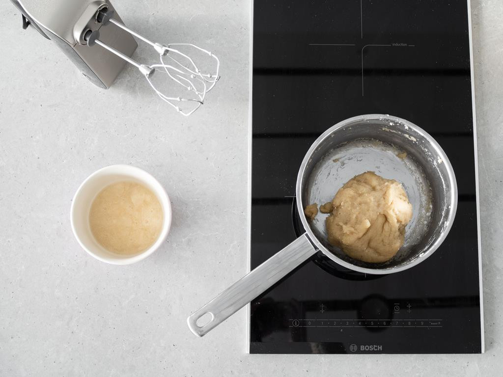 Aquafaba w miseczce oraz zaparzone ciasto wegańskie. Obok mikser ręczny firmy Bosch.