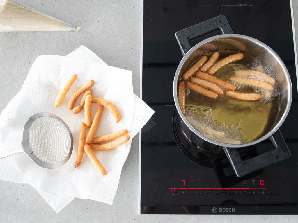 Smażenie churros w garnku. Obok na talerzyku churros odsączone na ręczniku papierowym.
