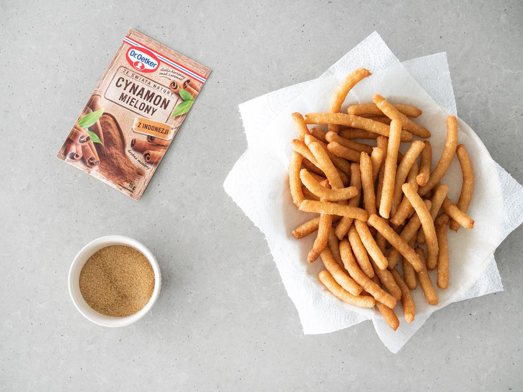Odsączone churros na ręczniku papierowym. Obok cynamon mielony i cukier trzcinowy.