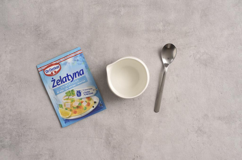 Żelatyna Dr. Oetker na blacie, obok woda.