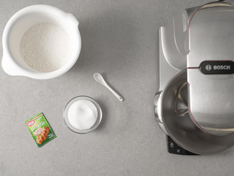 Robot kuchenny firmy Bosch, obok w misce mąka pszenna, cukier w miseczce, sól na łyżeczce i opakowanie drożdży suszonych instant Dr. Oetkera