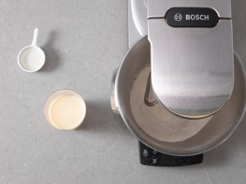 Robot kuchenny firmy Bosch, obok ciepły napój sojowy w szklance i rozpuszczony olej kokosowy.