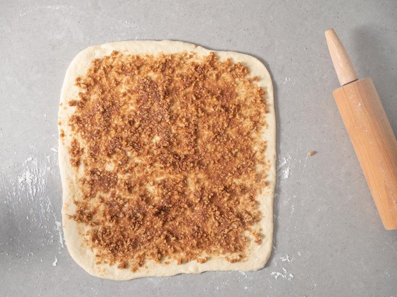 Rozsmarowane nadzienie cynamonowe na rozwałkowanym cieście drożdżowym.
