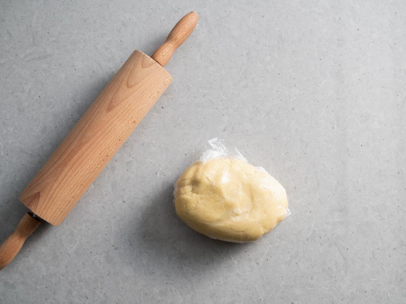 kruche ciasto owinięte w folię spożywczą obok wałek do ciasta