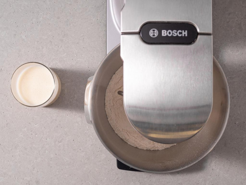 Suche składniki w misie miksera kuchennego firmy Bosch. Obok napój sojowy w szklance.