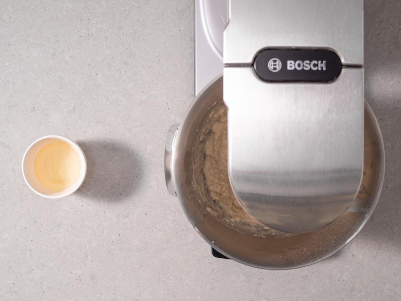 Robot kuchenny firmy Bosch wyrabiający ciasto drożdżowe. Obok rozpuszczony olej kokosowy w miseczce.