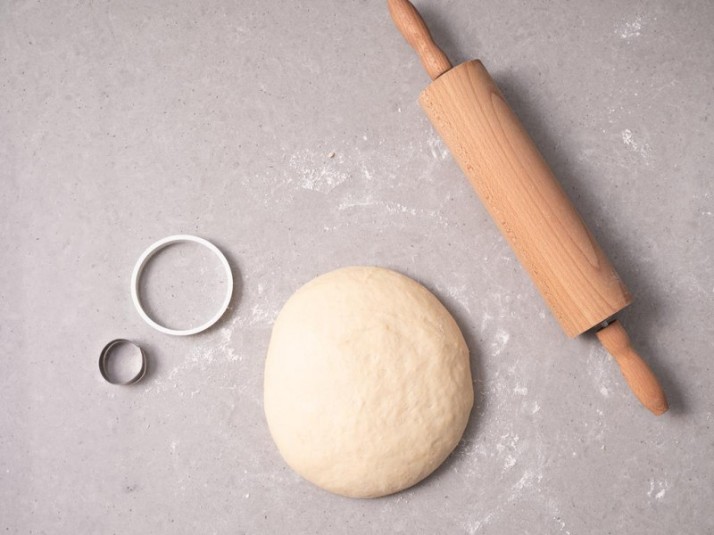 Zagniecione ciasto na oponki na blacie. Obok wałek do ciasta i dwie okrągłe wykrawaczki do ciast.