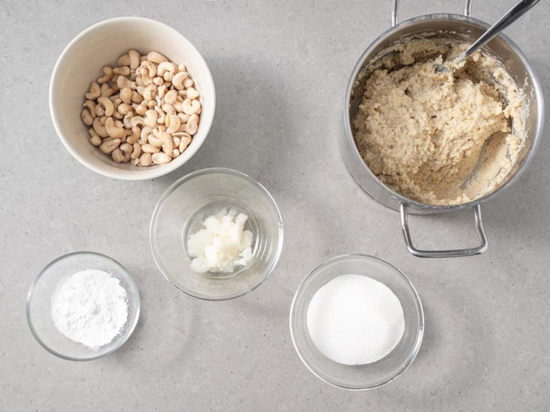 Ugotowana kasza w garnku, obok orzechy nerkowca, w miseczce olej kokosowy, cukier oraz budyń.