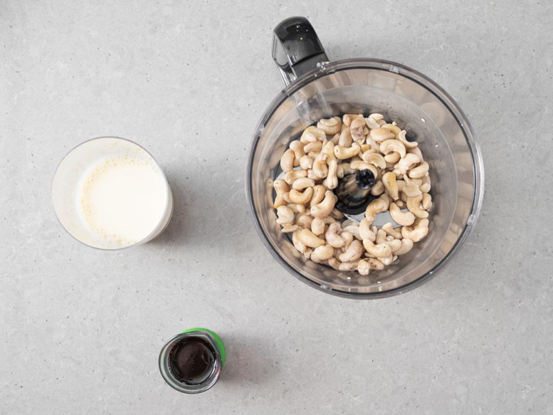 Odsączone orzechy nerkowca w malakserze. Obok syrop klonowy i napój sojowy.