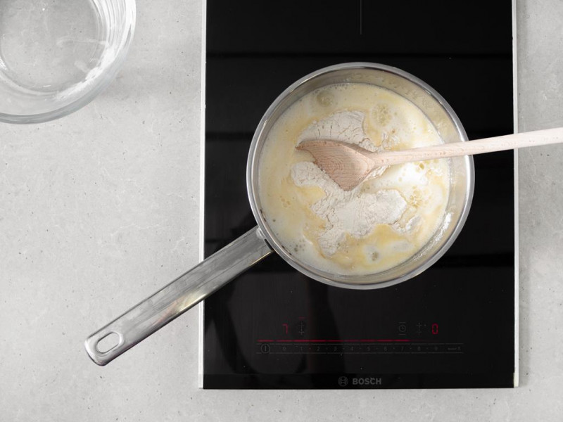 Na płycie indukcyjnej firmy Bosch garnek z gotującą się wodą, masłem i mąką.