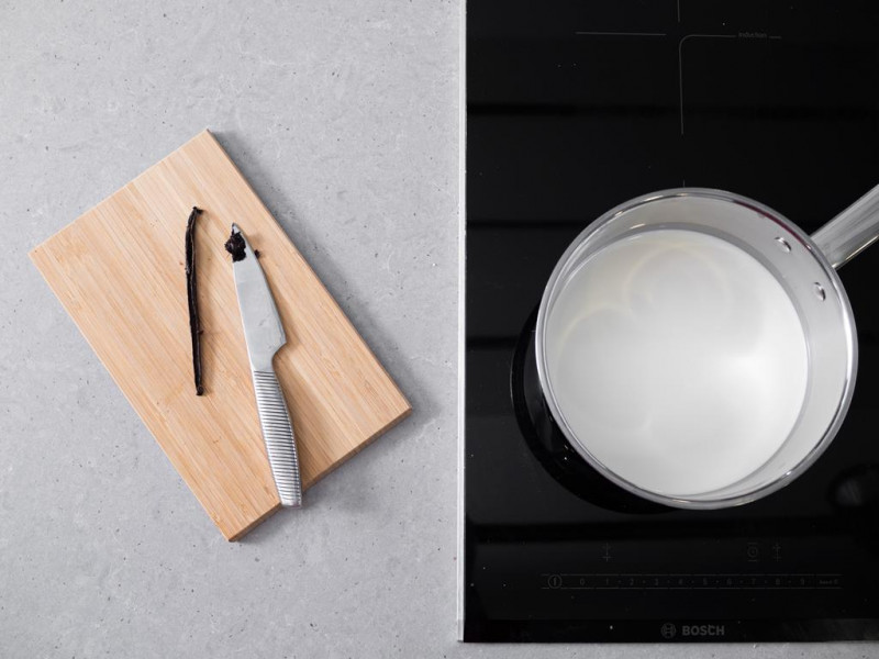 Mleko w garnku i przecięta laska wanilii na drewnianej desce.