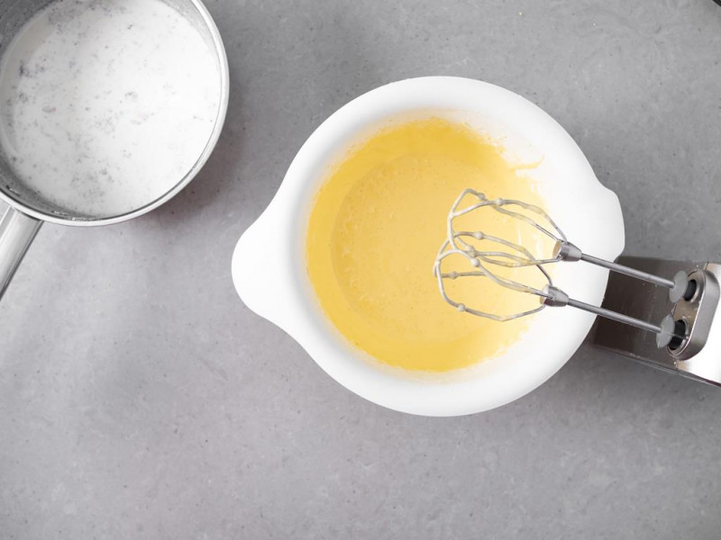 Żółtka utarte z cukrem. Obok podgrzanego mleko z wanilią.