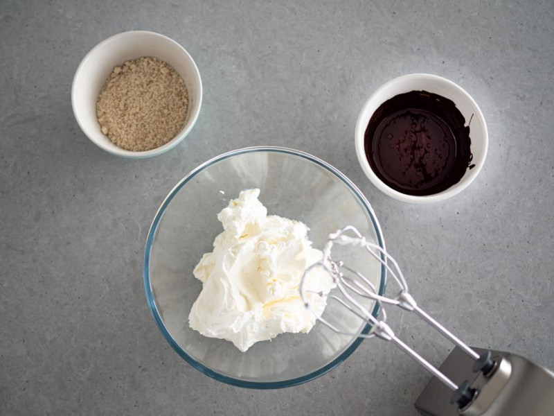 ubita śmietanka z serkiem mascarpone. zmielone migdały. roztopiona czekolada w miskach
