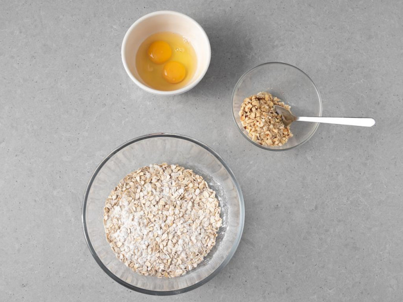 W misie wymieszane suche składniki. Obok w miseczce posiekane orzechy laskowe i 2 jajka.