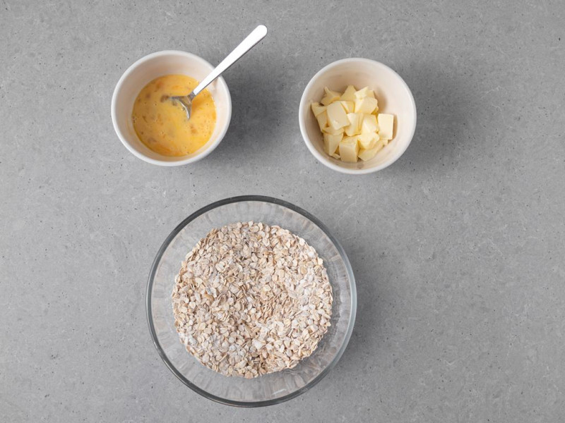 W misie wymieszane suche składniki wraz z orzechami laskowymi. Obok w miseczkach miękkie masło i 2 jajka.