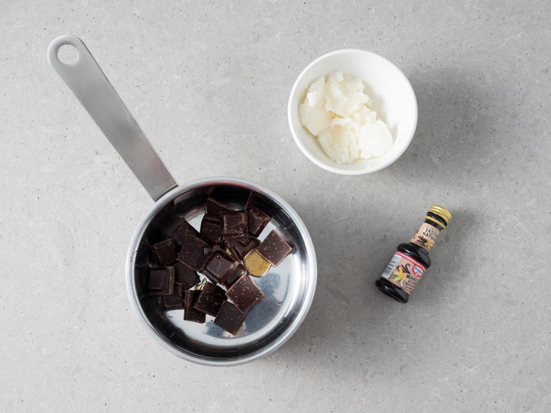 Kawałki czekoladowy w garnuszku. Obok ekstrakt z wanillii Dr. Oetkera i olej kokosowy w miseczce.