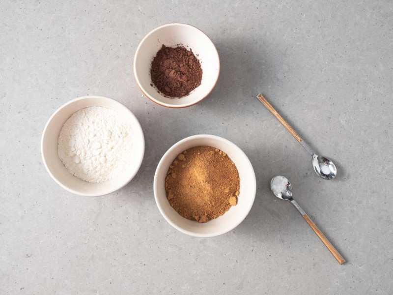 W miseczkach mąka pszenna, kakao oraz cukier. Obok na łyżeczkach sól i soda.