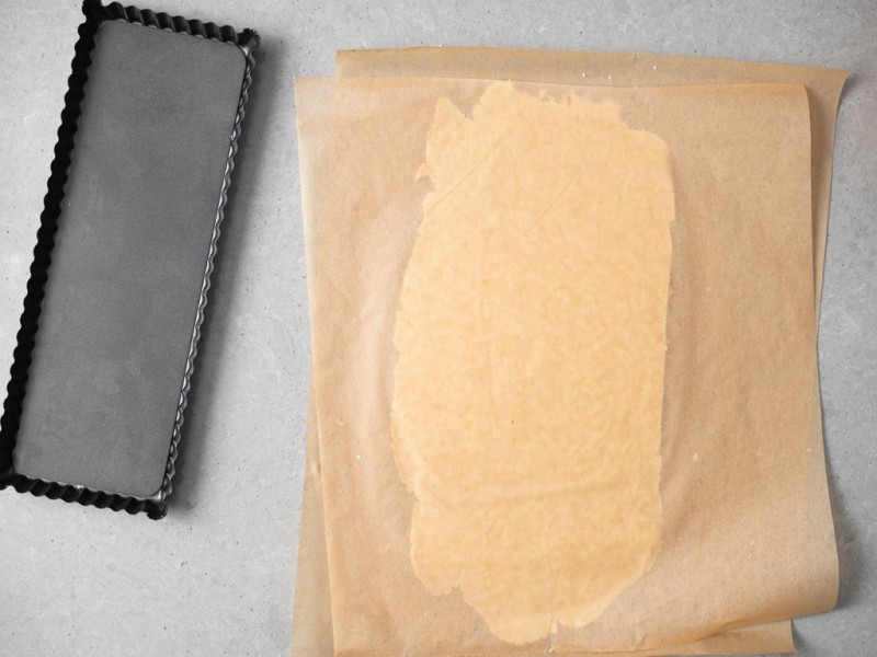 Kruche ciasto wegańskie rozwałkowane pomiędzy arkuszami papieru do pieczenia.