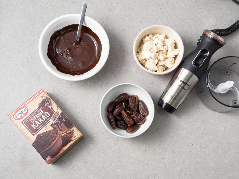 Ciemne kakao Dr. Oetker, daktyle, rozpuszczona czekolada i rozkruszone tofu w miseczkach. Obok blender ręczny firmy Bosch.