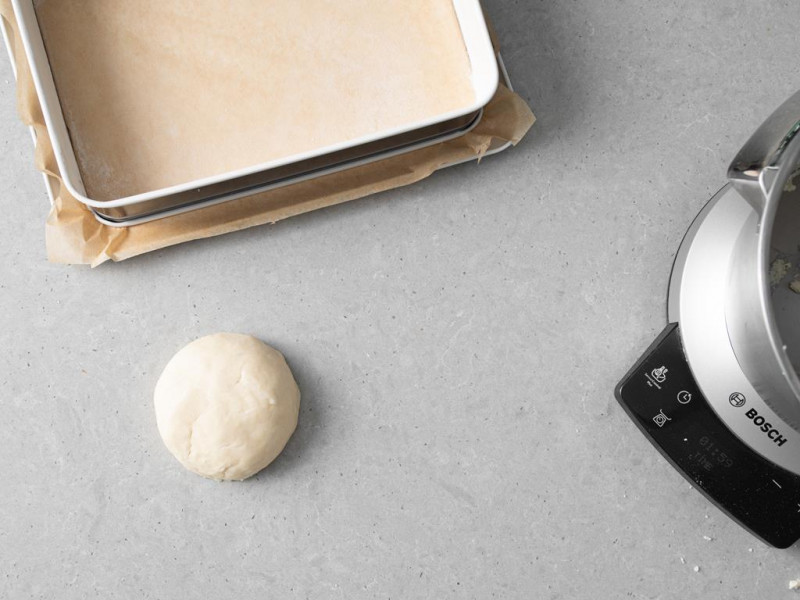 Zagniecione ciasto kruche. Obok foremka wyłożona papierem do pieczenia.