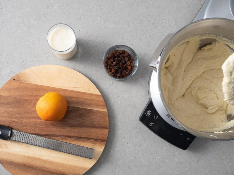 Na desce pomarańcza. Obok rodzynki, napój sojowy i masa tofurnikowa w misie.