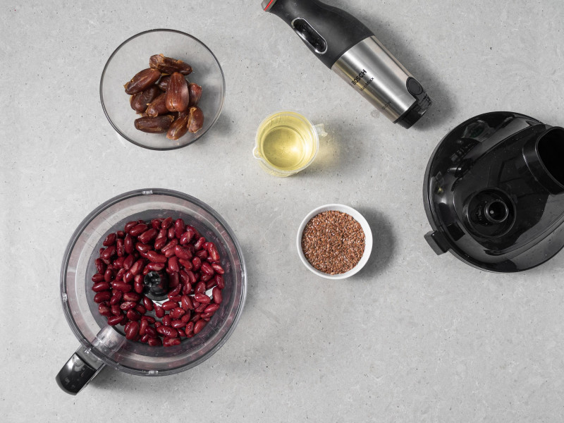 Fasola w pojemniku malaksera. Obok w miseczkach siemię lniane, olej rzepakowy i daktyle.