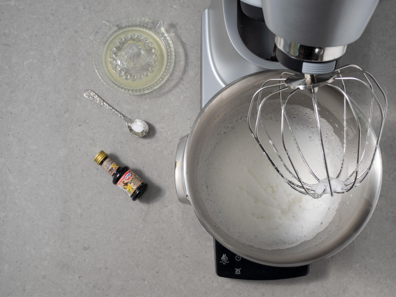 W misie robota kuchennego spienione białka. Obok ekstrakt z wanilii, sól i sok z cytryny w miseczce.