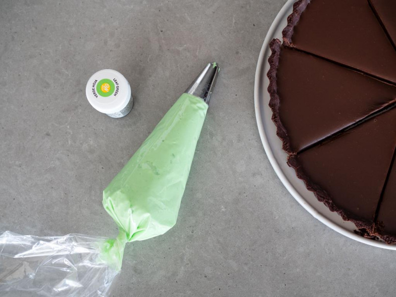 zielony krem miętowy z worku cukierniczym, obok barwnik spożywczy zielony listek marki Wilton oraz tarta czekoladowa