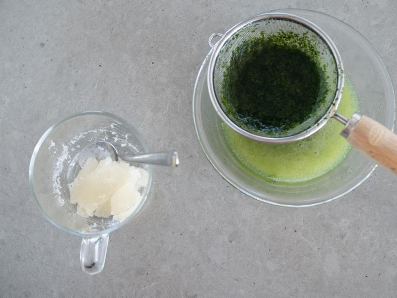 kisiel z listkami mięty zblendowany i przecedzony przez sitko do szklanej miski, obok żelatyna namoczona w wodzie w szklance z łyżeczką