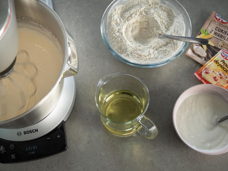 na blacie robot kuchenny bosch z ubijanym ciastem obok w naczyniach olej, mąka oraz jogurt naturalny