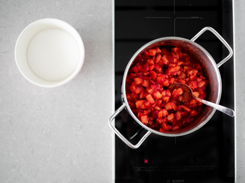 W garnku truskawki zagotowane z żelfixem. Obok w miseczce cukier.