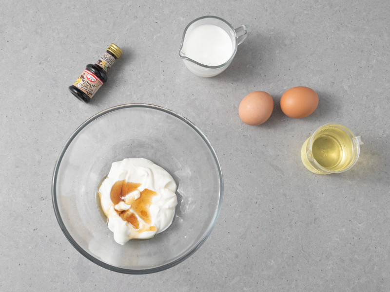 W misce kwa艣na 艣mietana z ekstraktem waniliowym. Obok jajka, olej, ekstrakt waniliowy Dr. Oetkera i mleko w dzbanuszku.