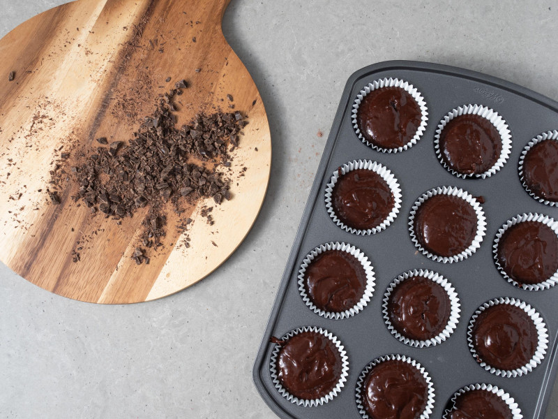 Posiekana czekolada na desce. Obok foremka na muffinki wype艂niona ciastem czekoladowym.