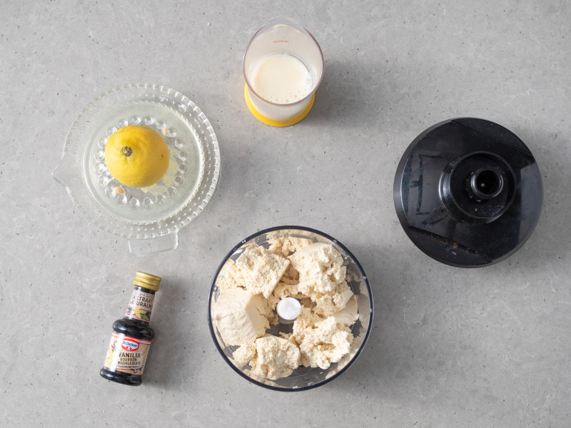 Przełożony do malaksera, pokruszony serek tofu. Obok ekstrakt naturalny Wanilia Dr. Oetkera, sok z cytryny i napój sojowy w szklanym naczyniu.