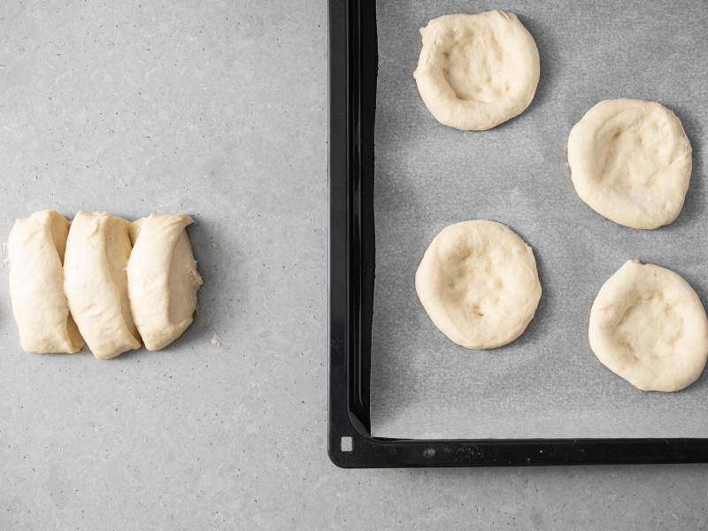 Na blasze placki z ciasta drożdżowego. Obok 3 kawałki ciasta na drożdżówki.