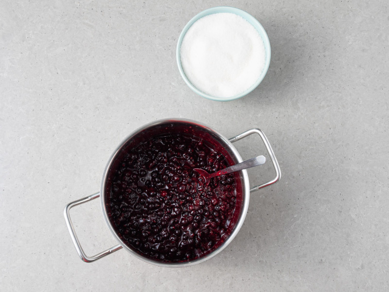 Czarna porzeczka zagotowana z żelfixem. Obok cukier w miseczce.